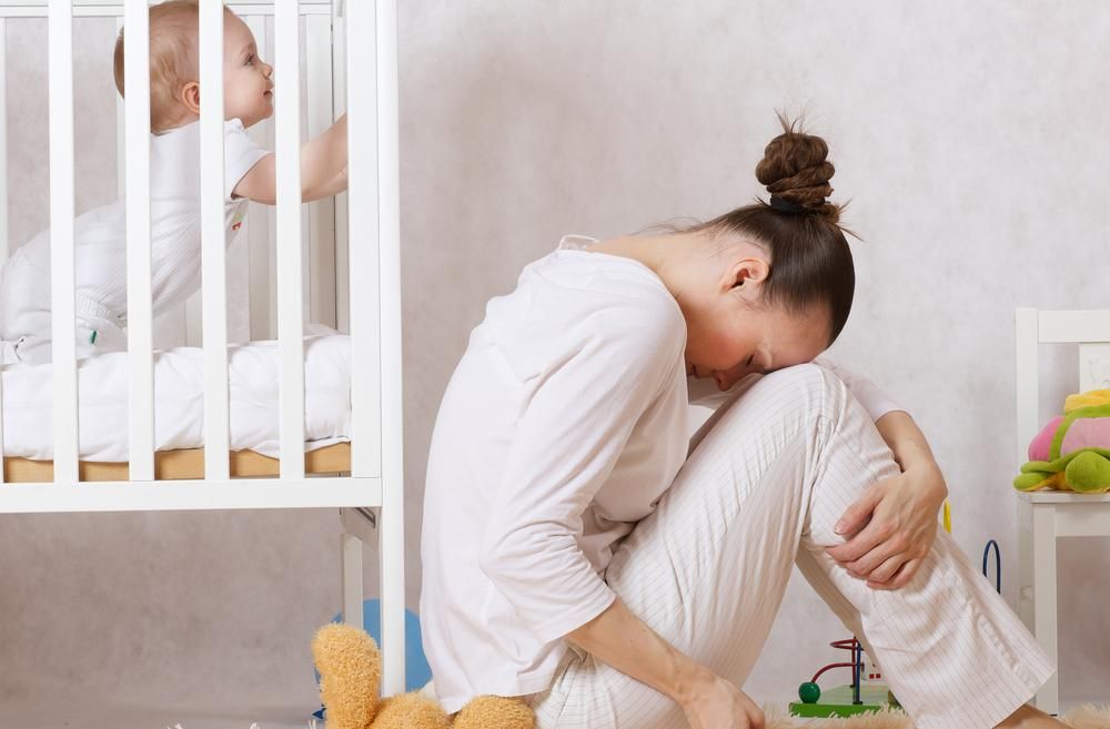 Kisbabája ágya mellett ülő anya szülés utáni depressziót tapasztal