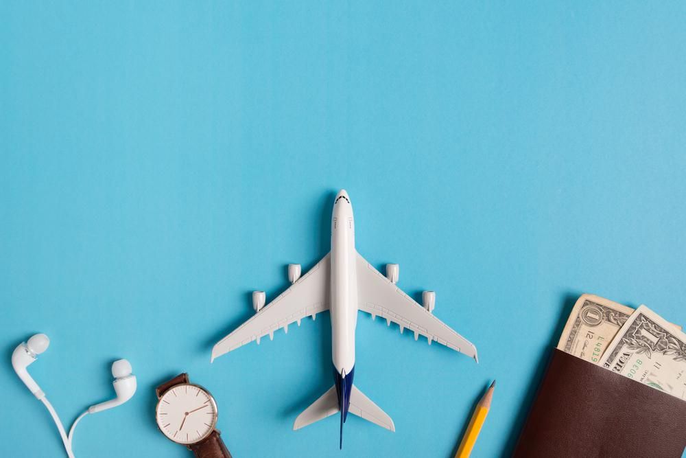 Fülhallgató, karóra, mini repülőgép, pénz, ceruza, kék háttér előtt - utazás koncepció