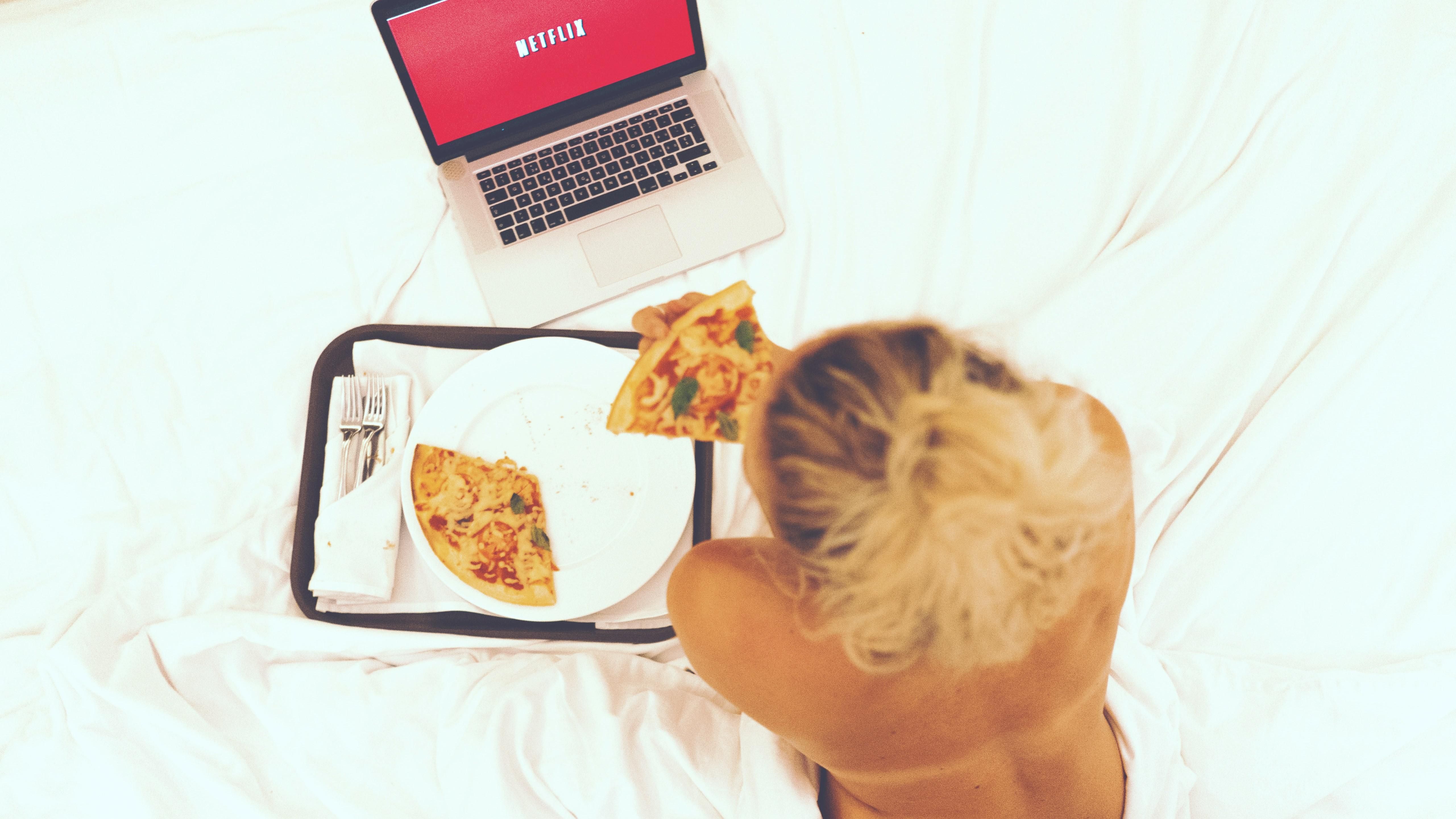 Egy lány az ágyában pizzát eszik Netflix nézés közben