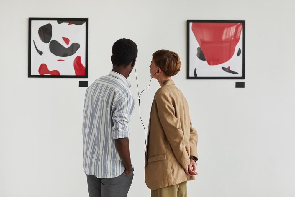 Férfi és nő festményeket nézegetnek és audio guide-ot hallgatnak együtt egy kiállításon