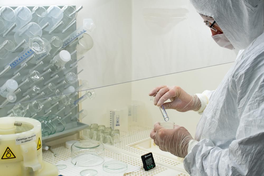 Fehér védőkabátban, maszkban és kesztyűben lévő tudós vírus- vagy baktériummintát elemez egy laboratóriumban fiolák, üveglombikok és vegyszerek segítségével. 
