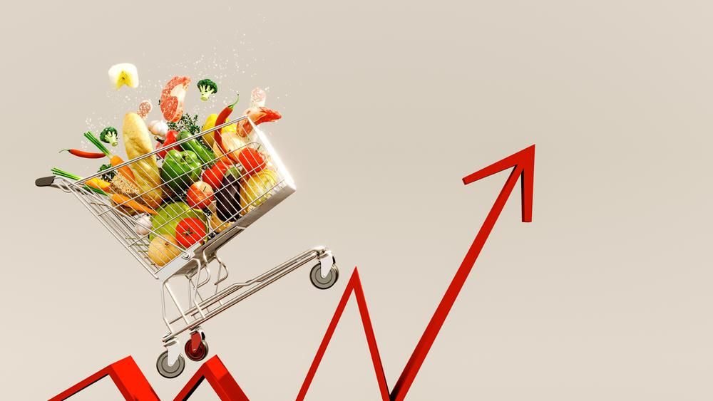 Bevásárlókocsi tele élelmiszerekkel, alatta felfelé mutató piros nyíl. Az élelmiszerárak emelkedő koncepciója. 