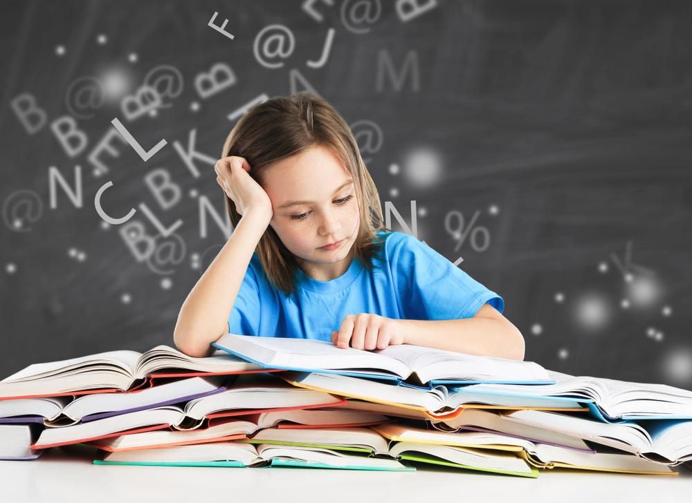 Diszlexiás kislány könyvek felett, körülötte különböző betűk a levegőben