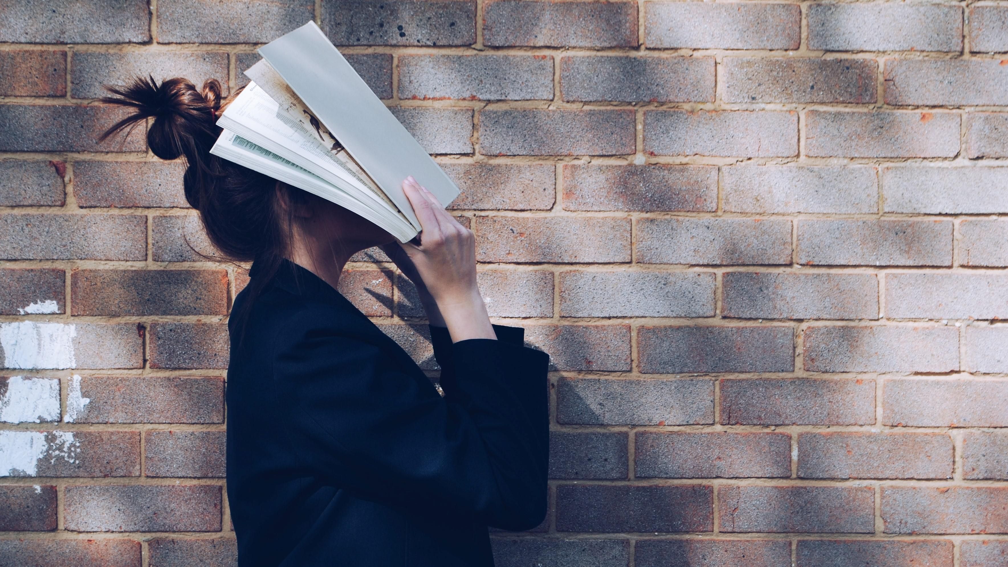 Egy lány könyvvel takarja az arcát