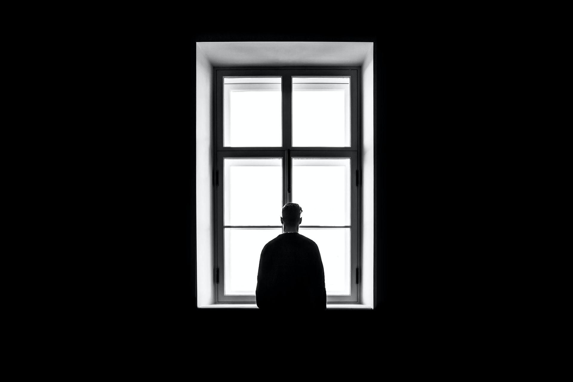 Ablakon kinéző férfi, sötét szobában