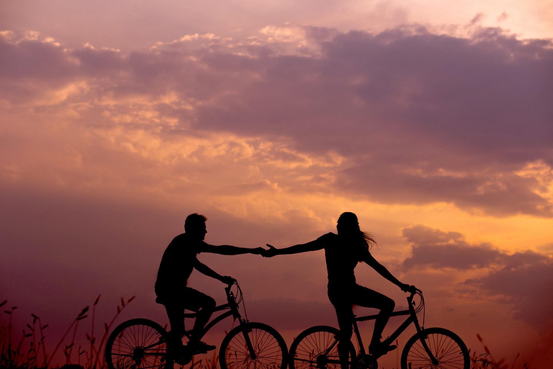 Bicikliző pár, egymáshoz nyúló kezek a naplementében