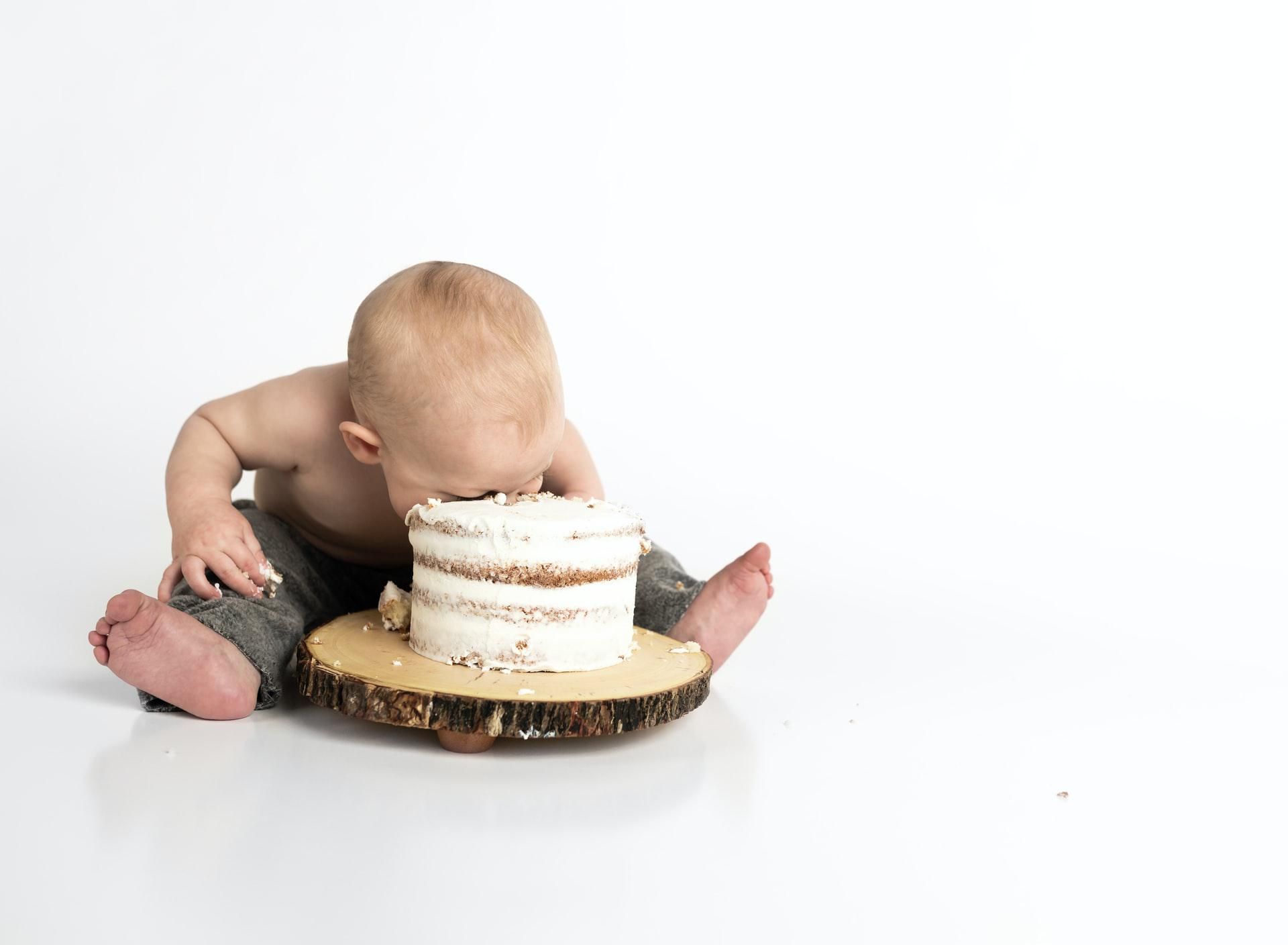 Fehér háttér előtt ülő kisbaba belefejel az előtte lévő tortába