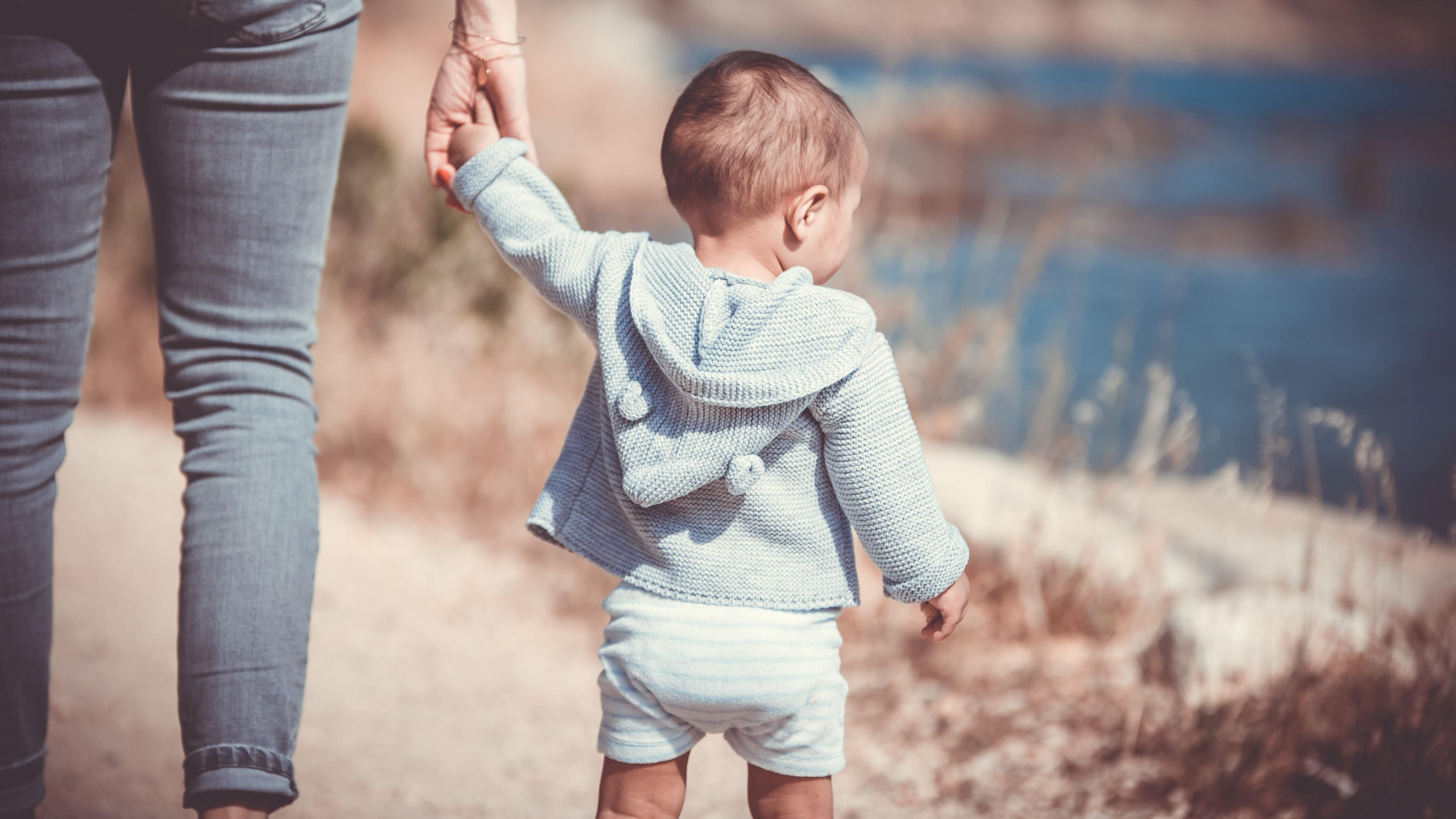 Egy kisgyerek az anyukája kezét fogja sétálás közben