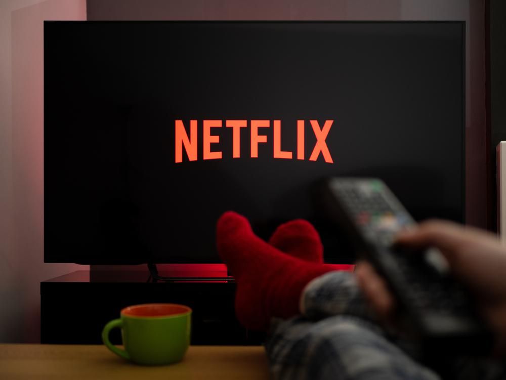 Asztalra feltett lábakkal a tévén Netflixet néző személy