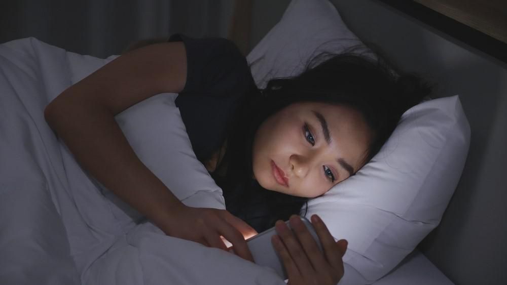Egy lány telefonozik az ágyában fekve