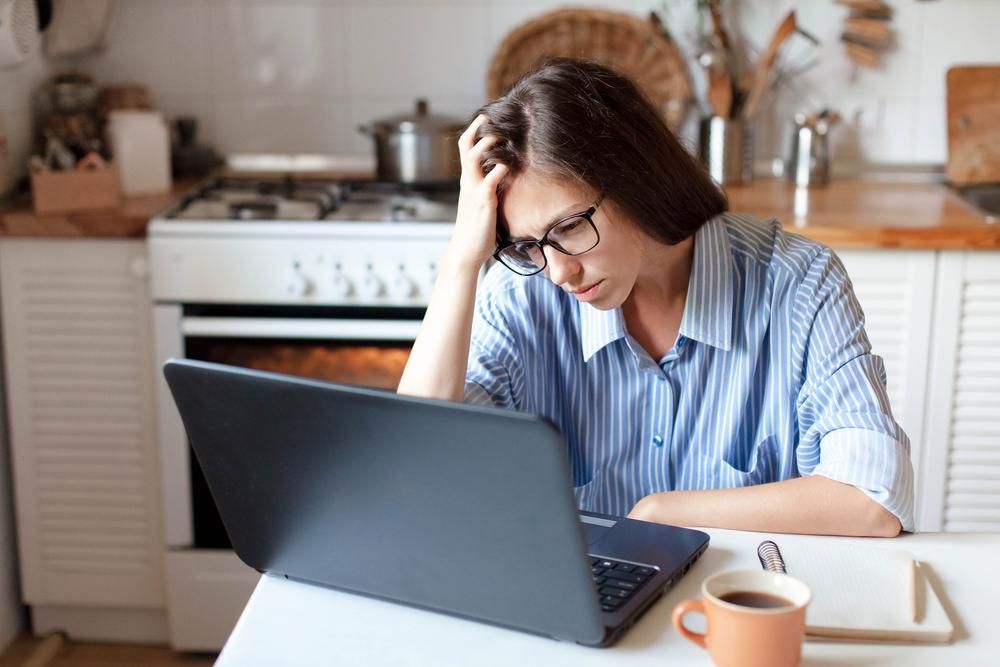 Otthonában dolgozó nő fáradtan nézi a laptopját
