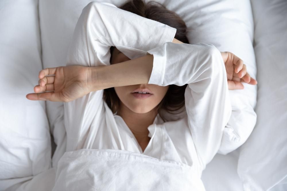 Álmatlanságtók kimerült fiatal nő fekszik az ágyban a paplan alatt, kezével eltakarja a szemét