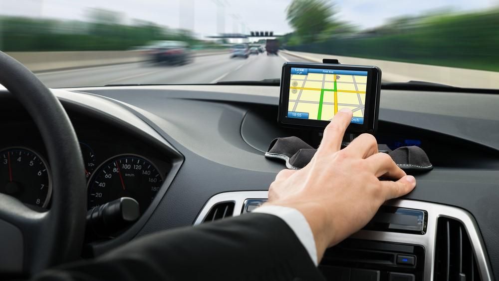 Egy ember a kocsijában lévő GPS-t állítja vezetés közben