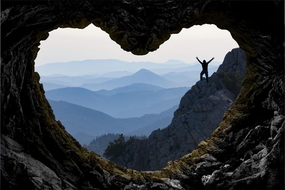Hegy tetejét megmászó ember sziluettje, szív alakú barlangnyílásból fényképzeve