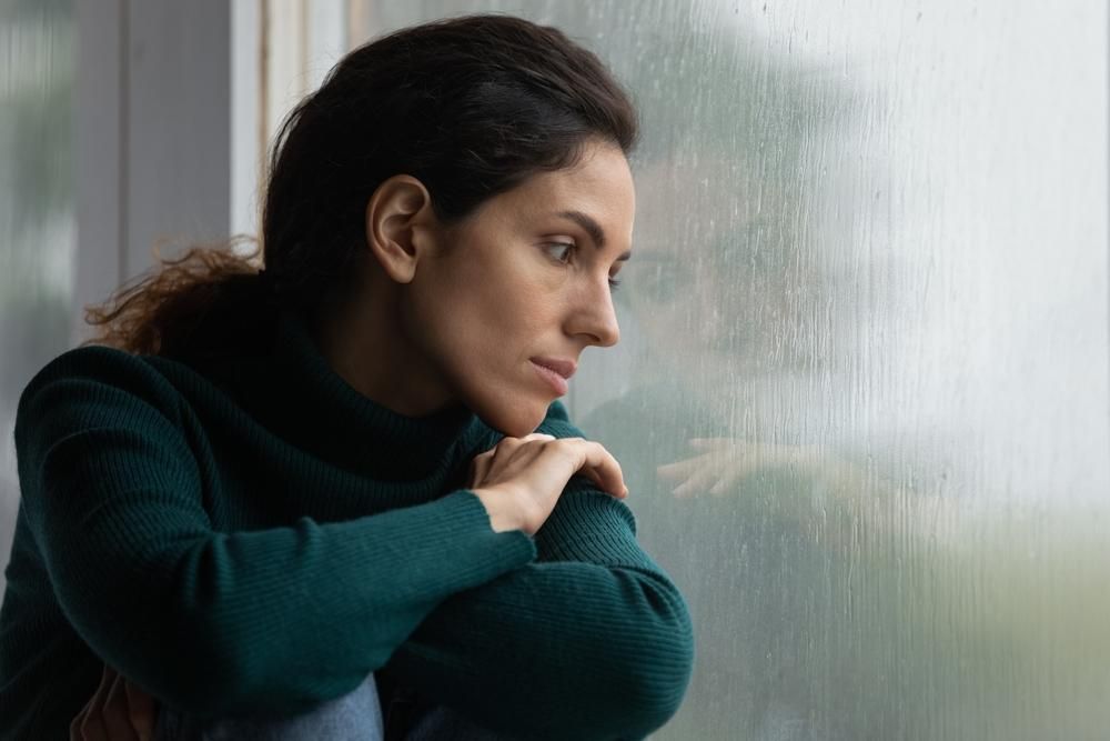 Depressziós vagy melankolikus hangulatban az ablaknál ülő nő, kint esik az eső