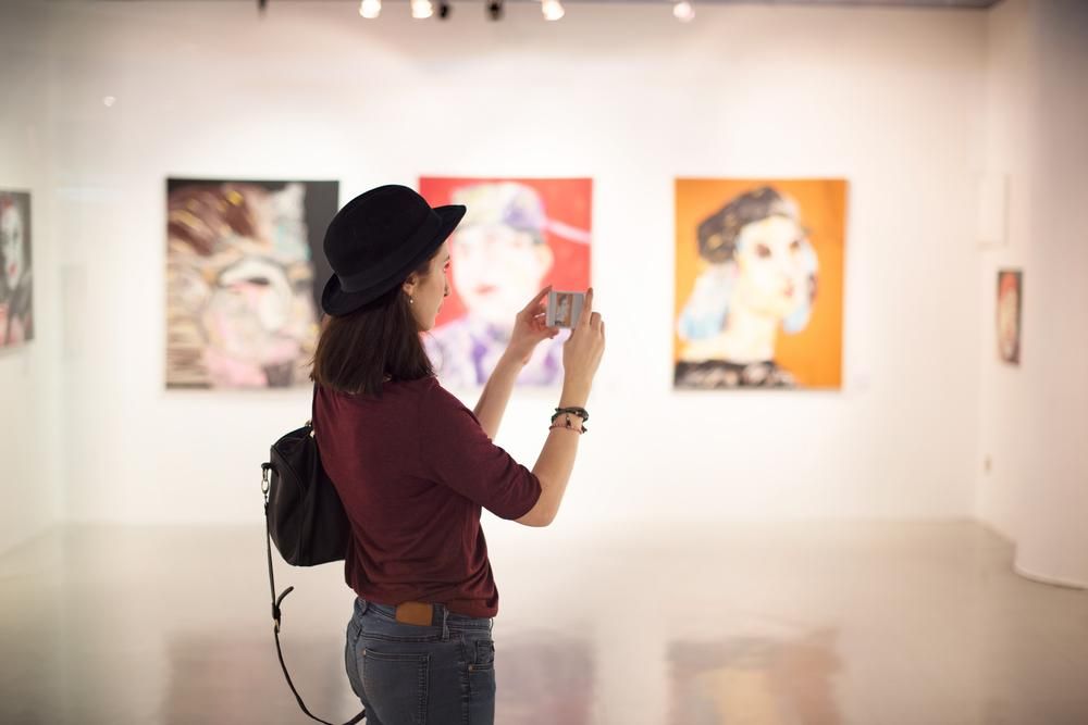 Nő kalapban áll egy művészeti galériában és fényképez