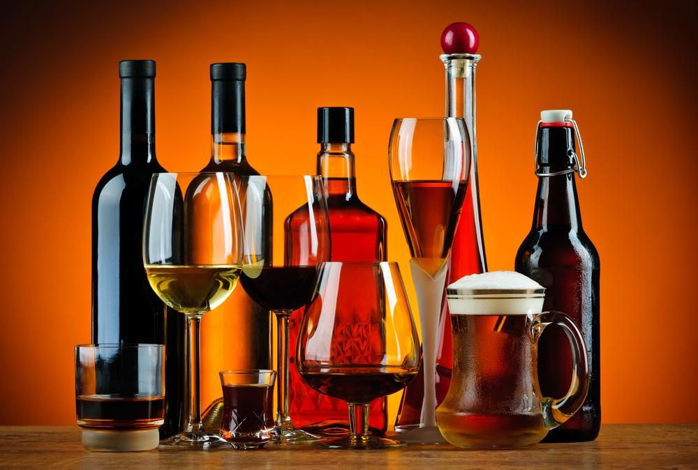 Különböző poharak és alkoholos italok narancsos színű háttér előtt