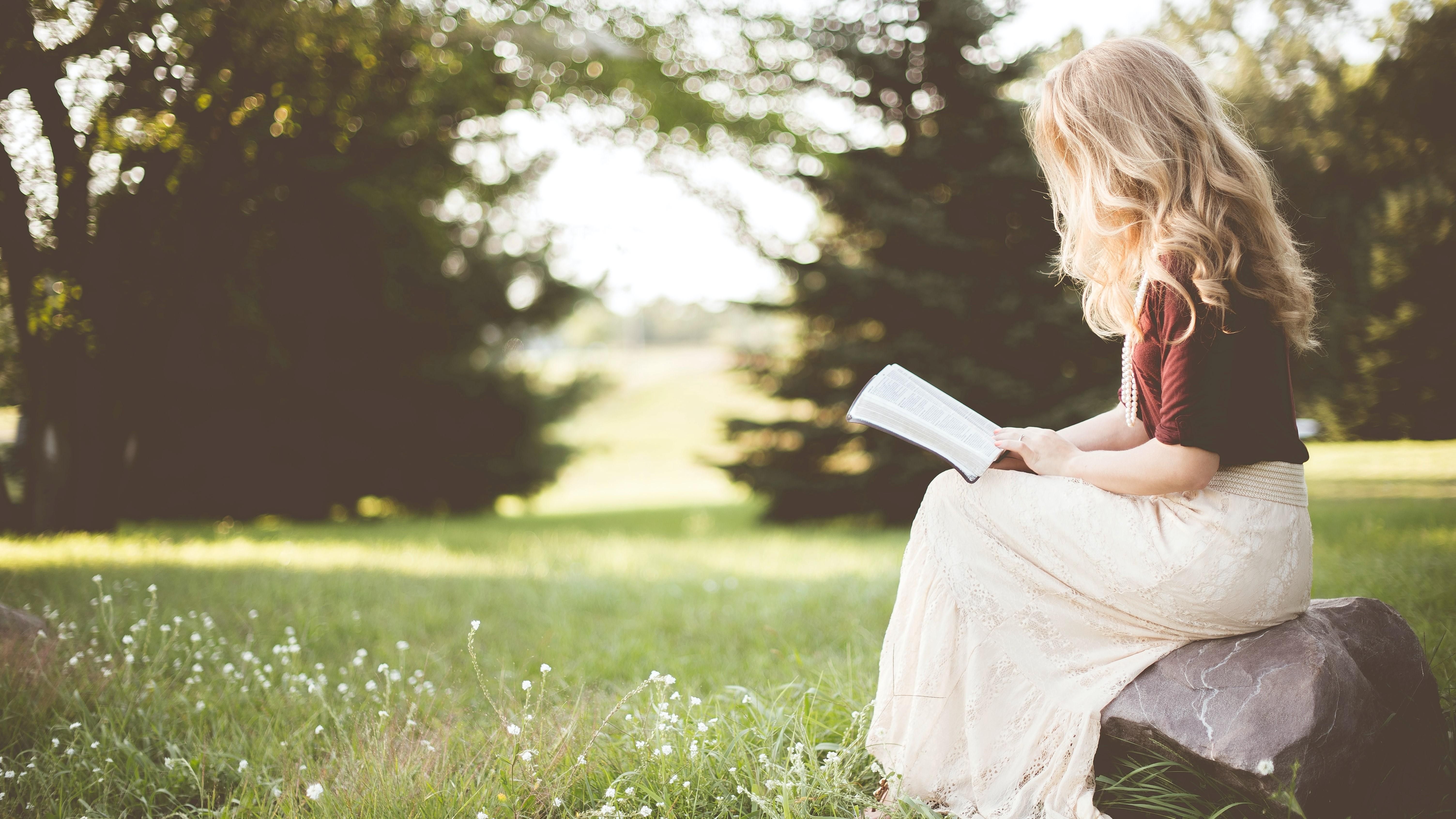 Egy szőke hajú lány könyvet olvas a természetben