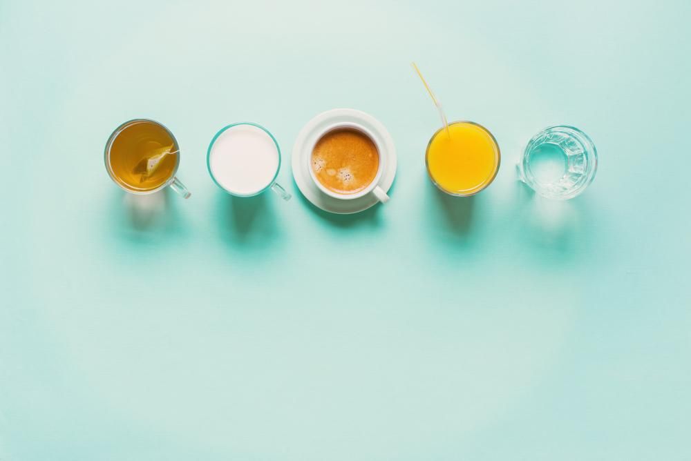 Különböző italok (tea, tej, kávé, narancslé és víz) kékeszöld háttéren