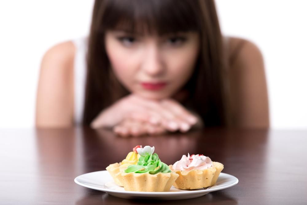 Egy tányér süti előtt ülő nő vágyakozik az édesség után