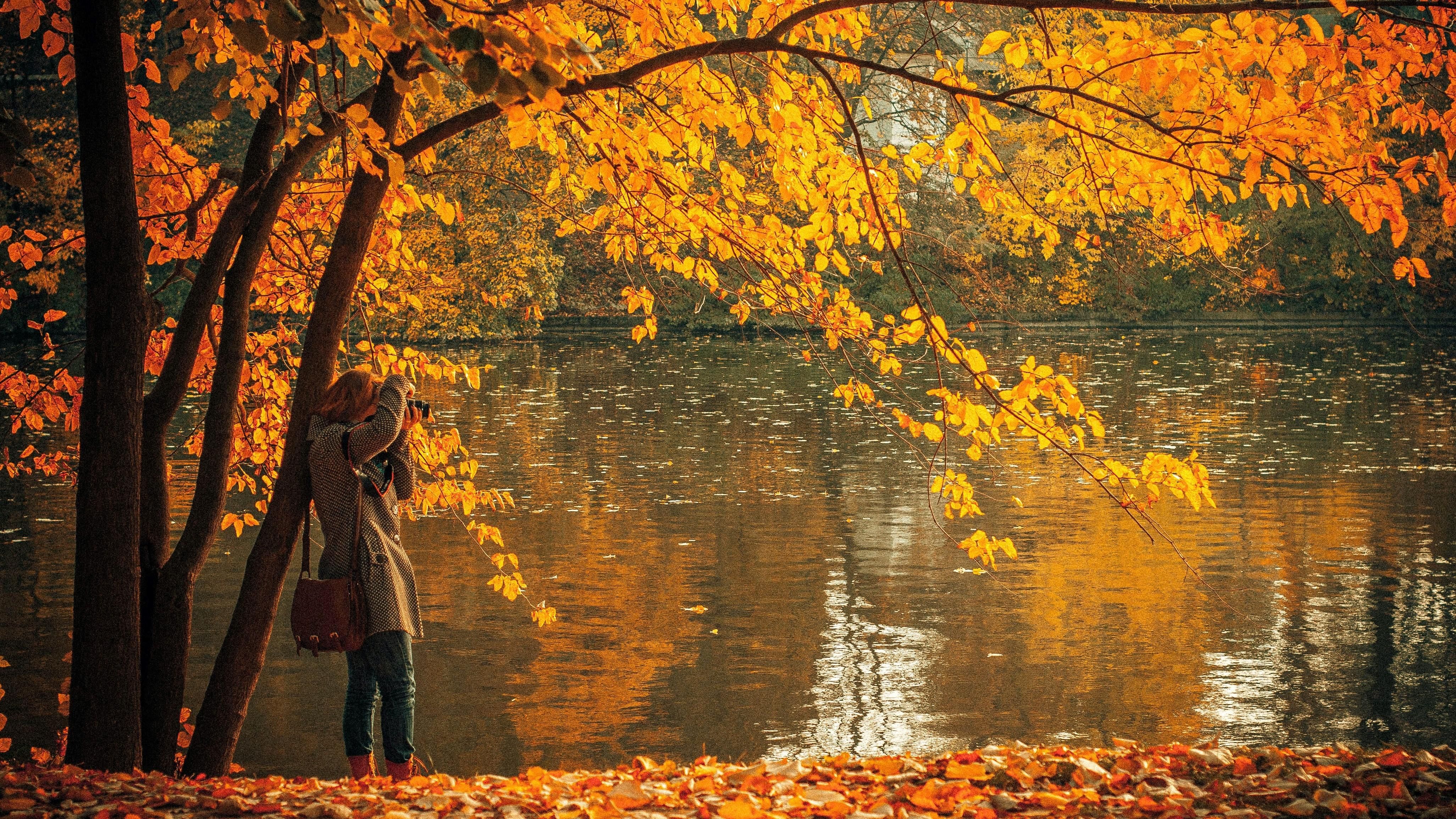 Egy lány egy tó mellett fotózza az őszi tájat