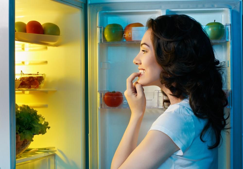 Hűtőben ételt keresgélő nő