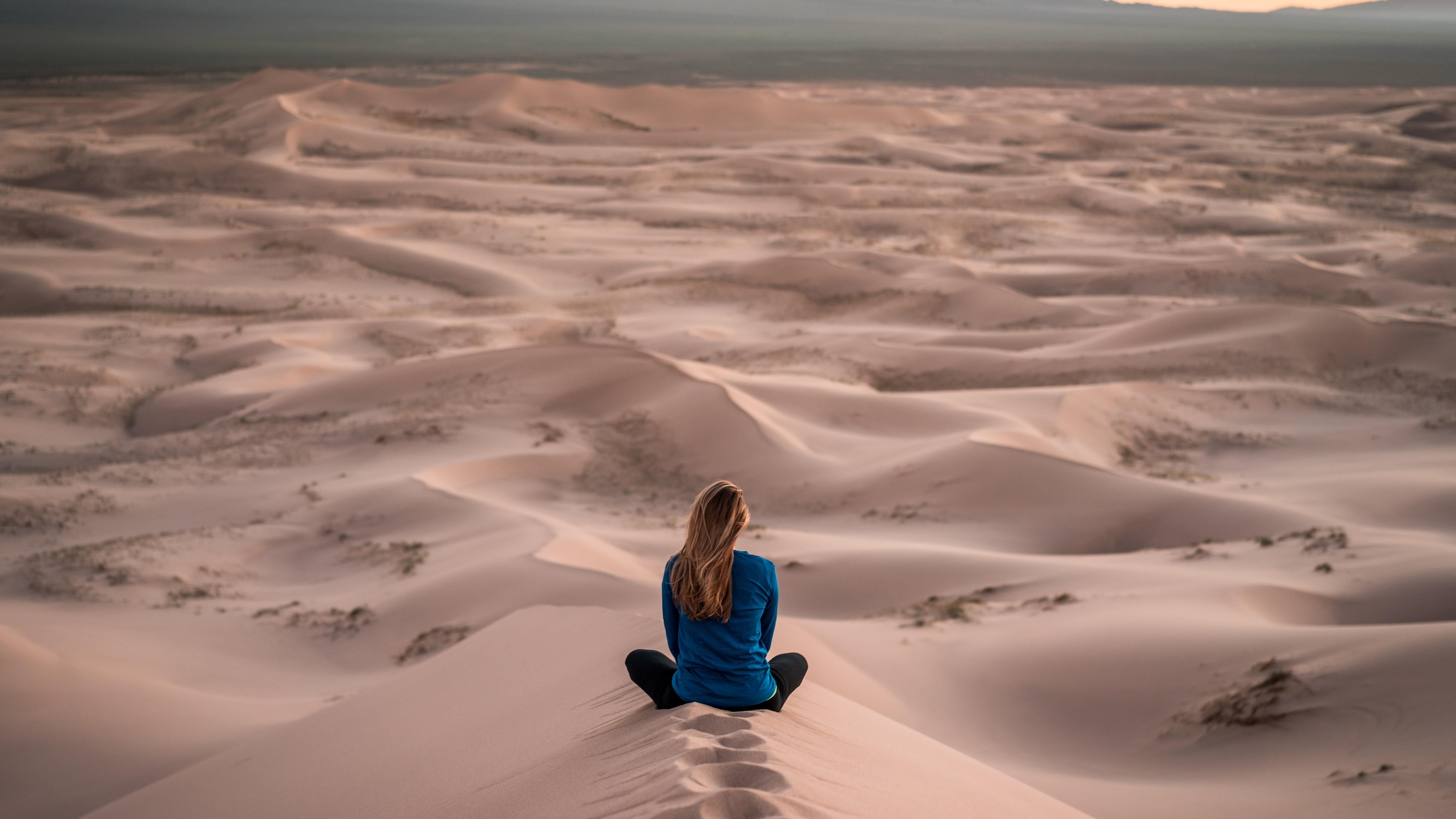 Egy lány egy homokdűnén ül a sivatag közepén