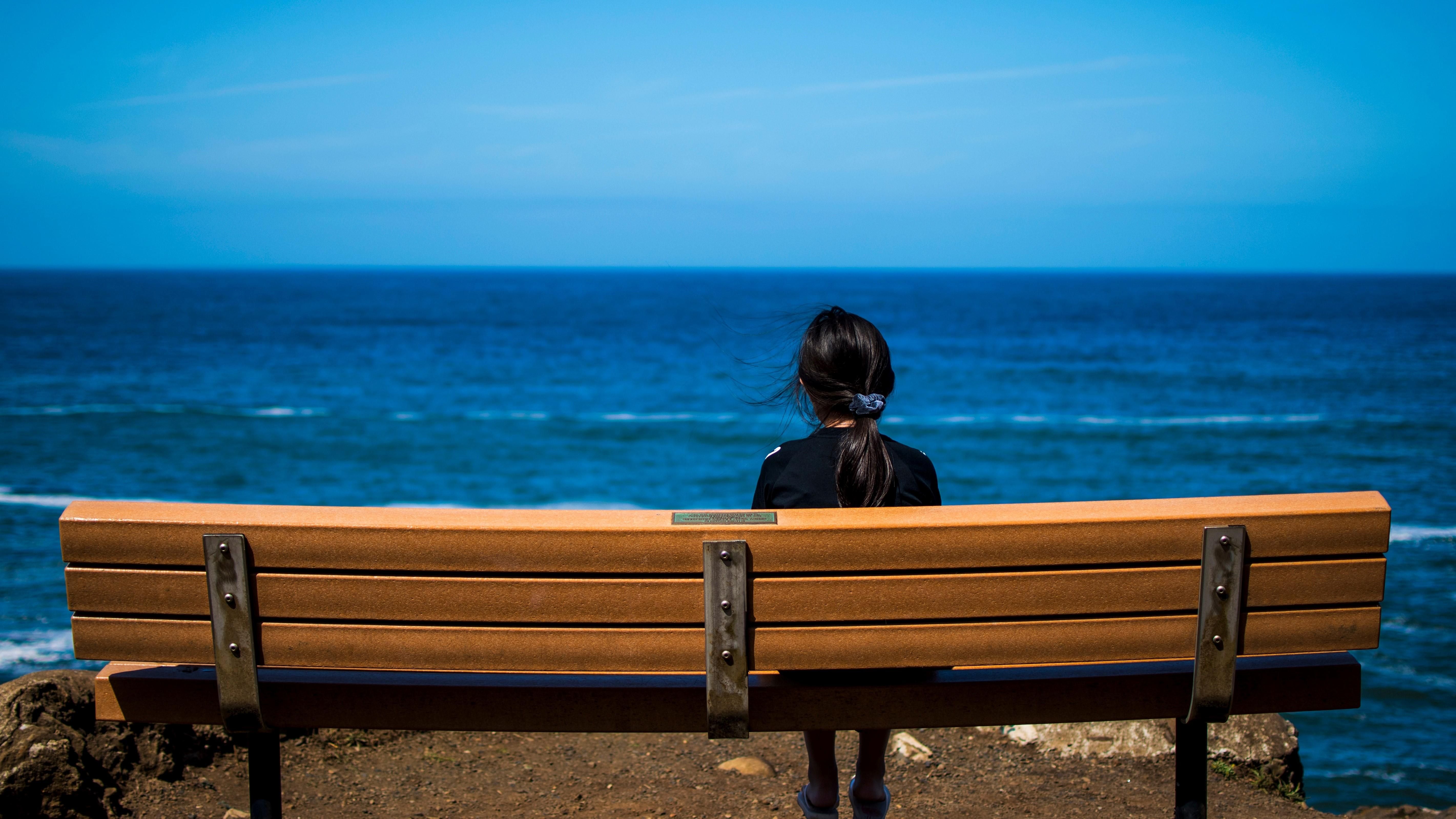 Egy lány egyedül ül egy hosszú padon