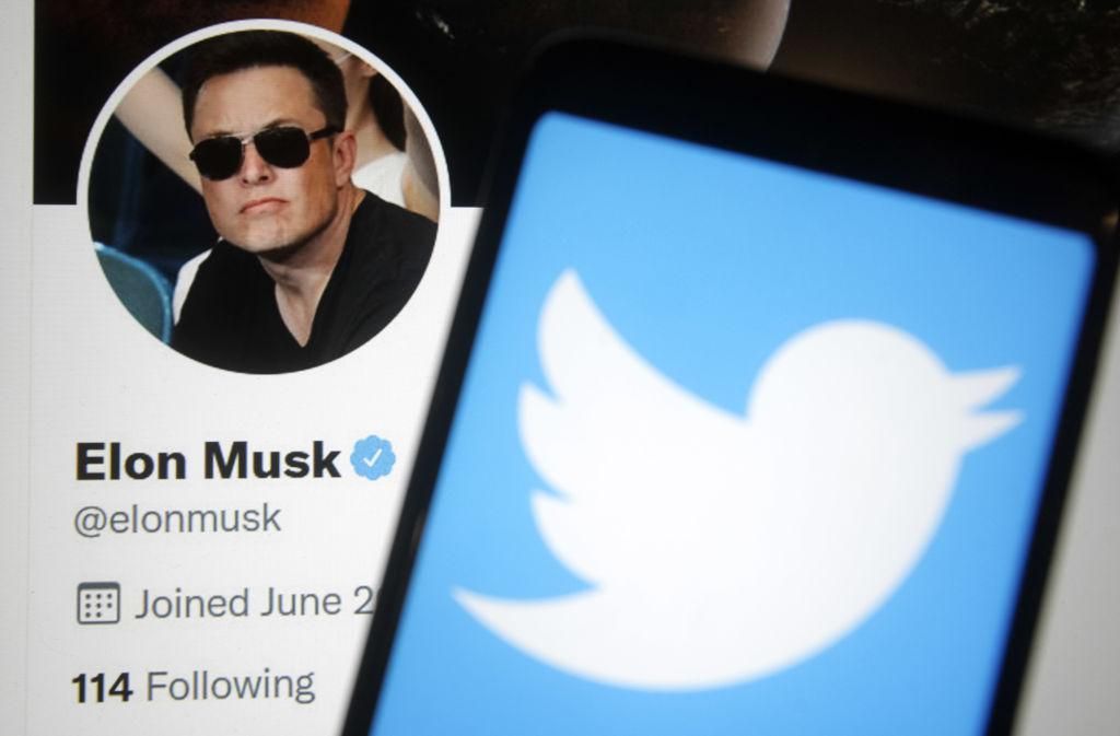 A Twitter logója egy okostelefon képernyőjén, a háttérben pedig Elon Musk Twitter weboldala