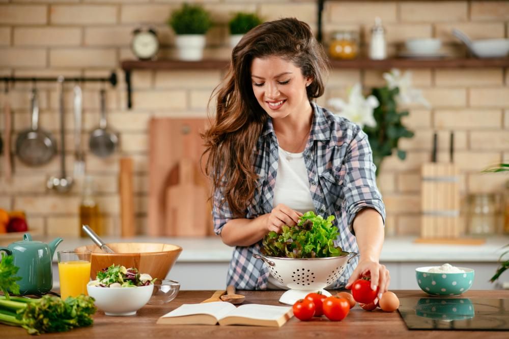 Nő salátát készít a konyhában, kockás ingben