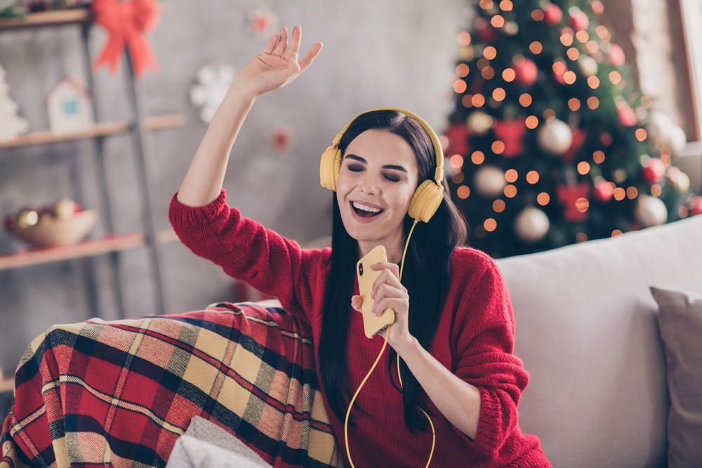 Piros pulcsiban énekel egy nő fejhallgatóval a fején, karácsonyfa a háttérben