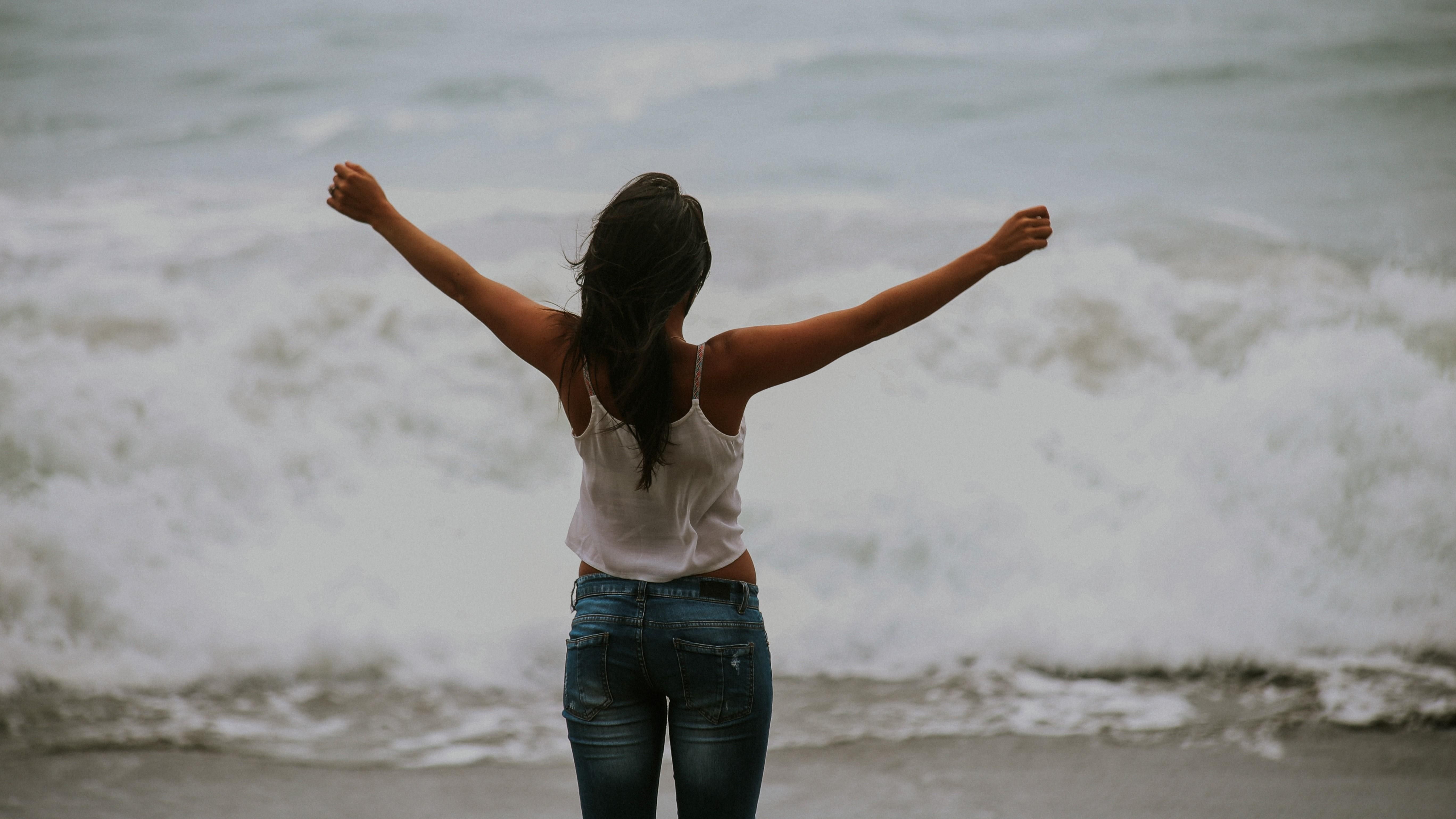 Egy lány tárt karokkal áll egy vízparton