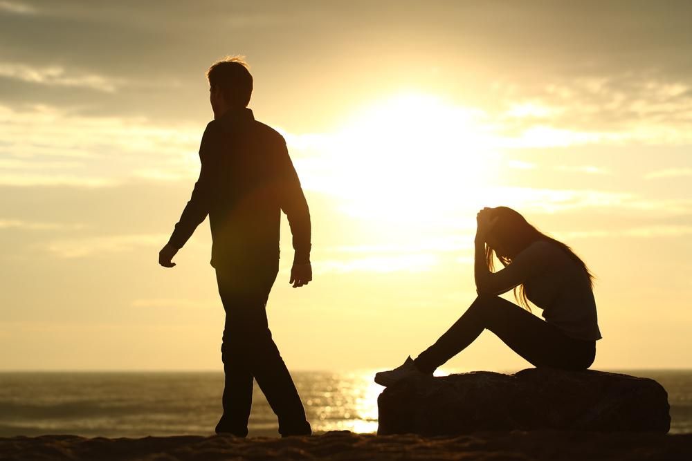 Férfi és női sziluett, férfi elsétál a nőtől a tengerparton naplementekor
