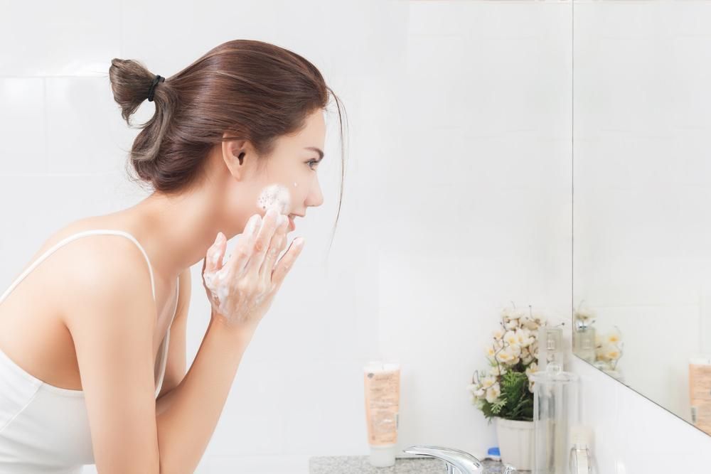 Barna hajú nő mossa az arcát a tükör előtt