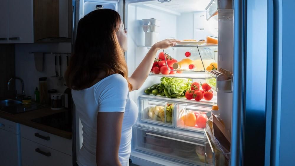 Egy nő éjjel kinyitja a hűtőjét