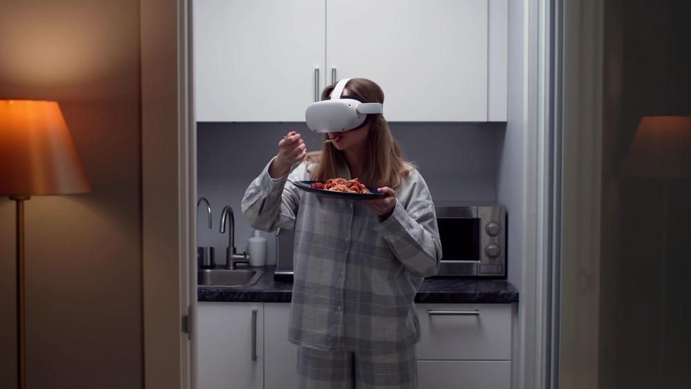 Egy lány tésztát eszik, miközben a fején egy VR-szemüveg van