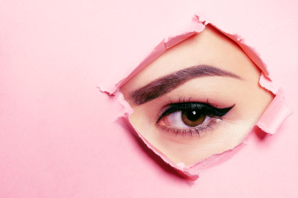 Rózsaszín papír lyukon néző női szem