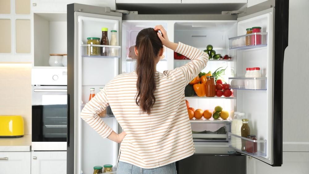 Egy nő gondolkodik a hűtőszekrénye előtt