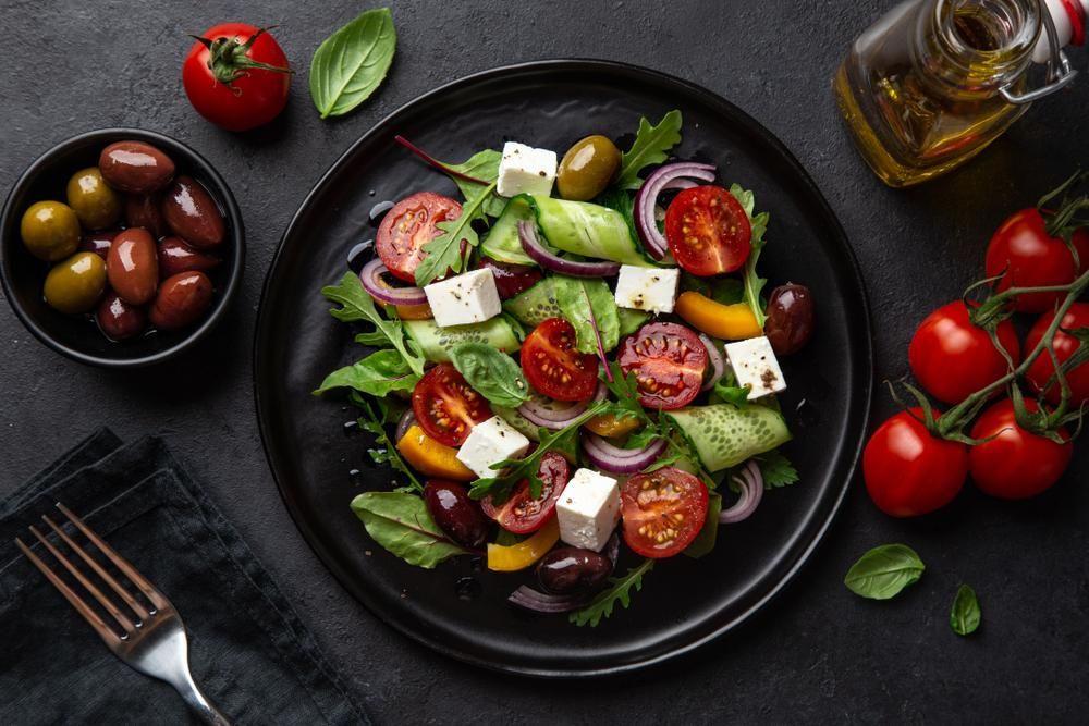 Friss görög saláta paradicsommal, uborkával, olajbogyóval és feta sajttal fekete tányéron