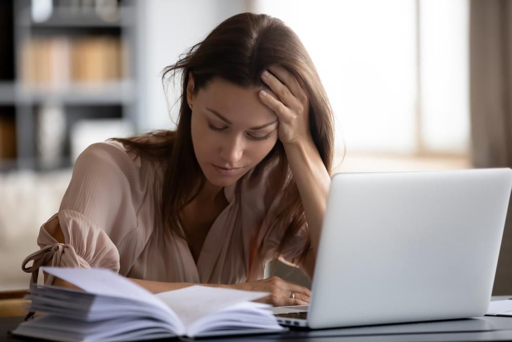 Kimerült nő laptop előtt, fejét kezében tartva