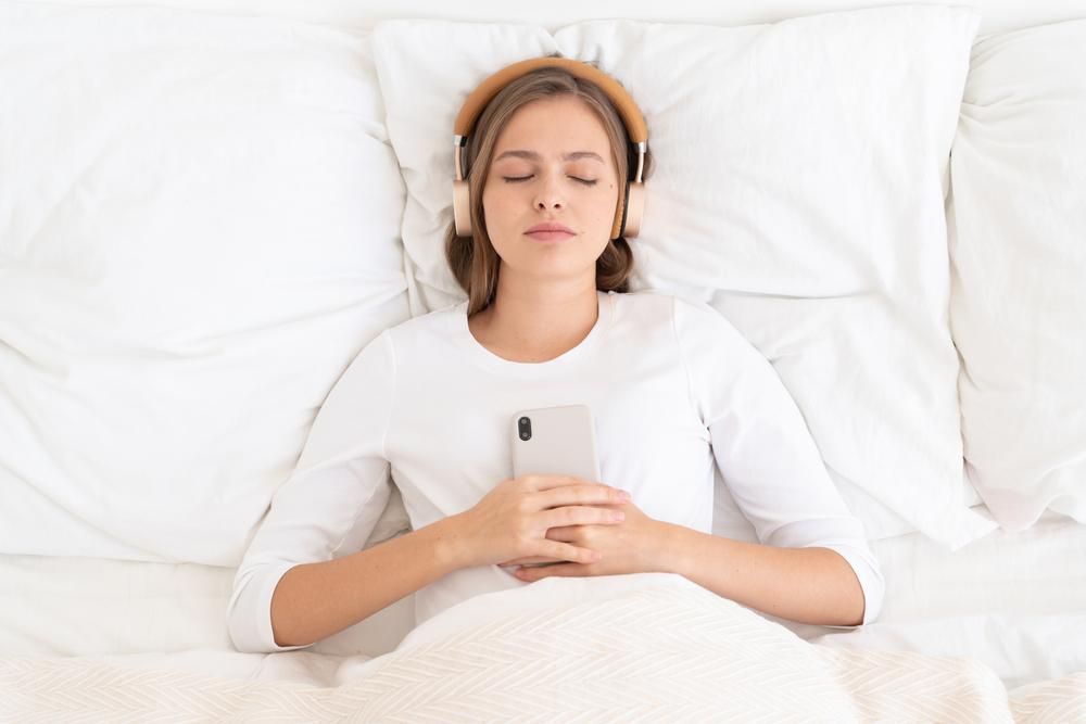 Fejhallgatóval alvó nő, kezében mobiltelefon