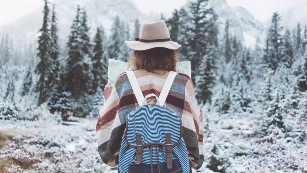 Egy hátitáskás túrázó a térképét nézi a havas táj előtt