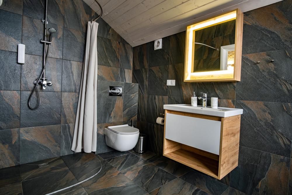Modern, stílusos fürdőszoba belső tere fekete csempézett falakkal, függönyös zuhanyzóval, fából készült bútorokkal, mosdókagylóval és nagy, megvilágított tükörrel