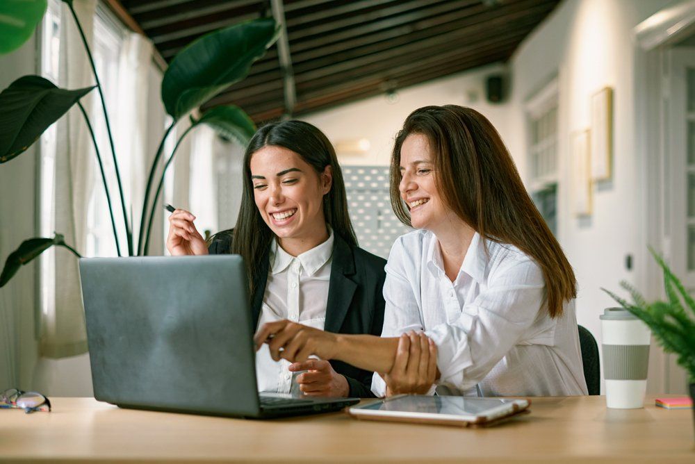 Női kollégák boldogan ülnek a laptop előtt