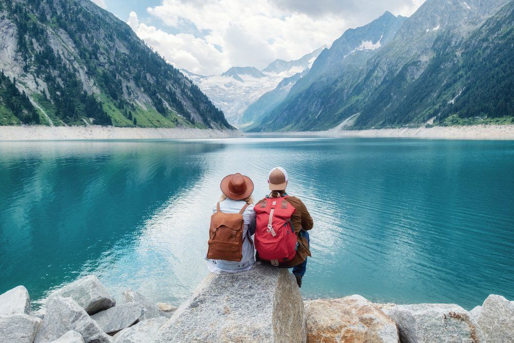 Hegyek övezte tó előtt ülő turista pár