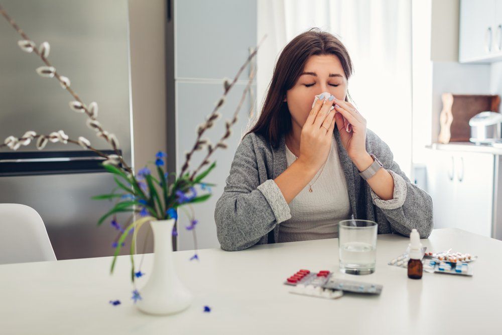 Allergiás nő ül az asztalnál gyógyszerek előtt és fújja az orrát