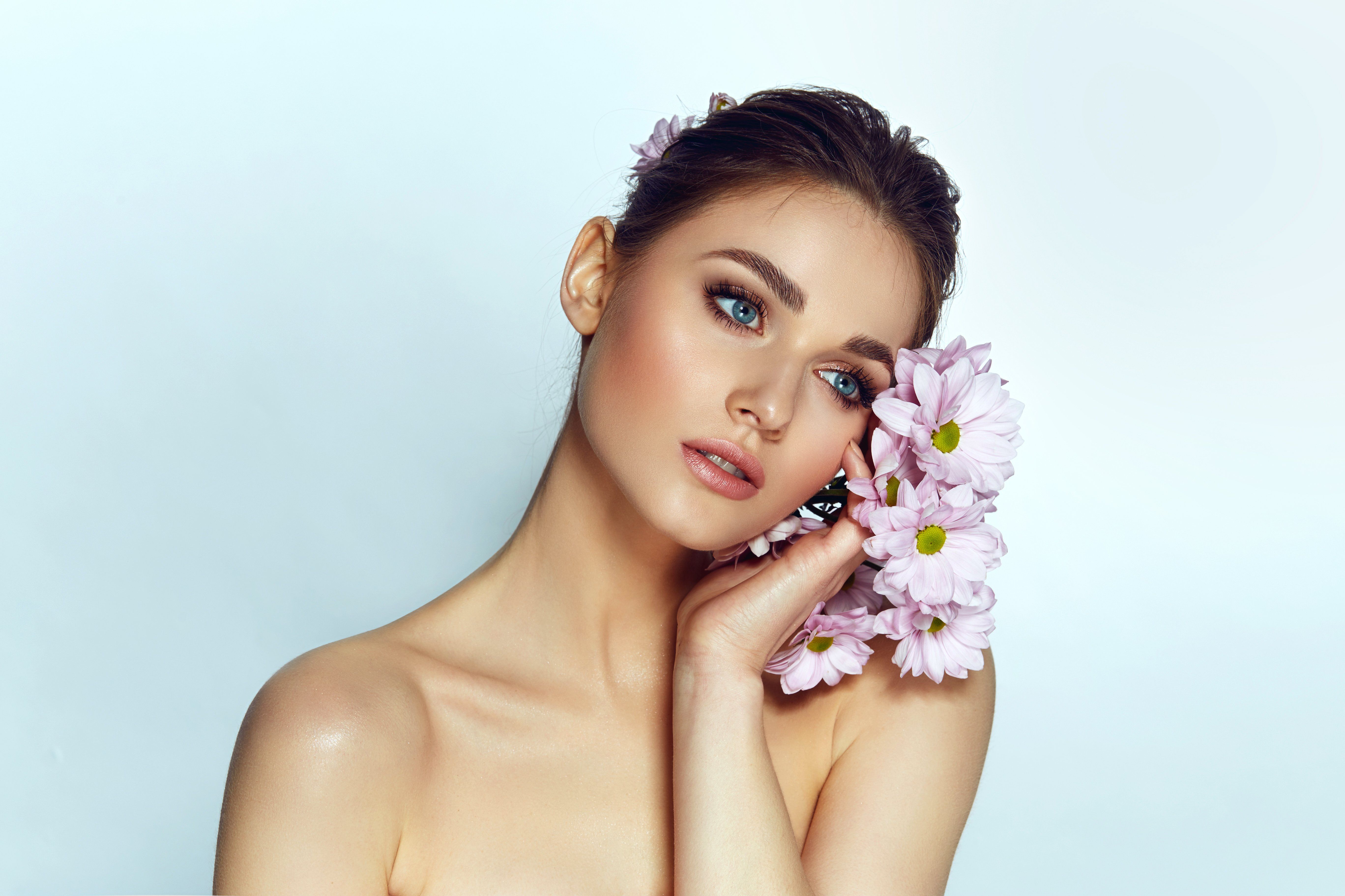 Gyönyörű fiatal nő sminkben virágokat tart az arcához, portré