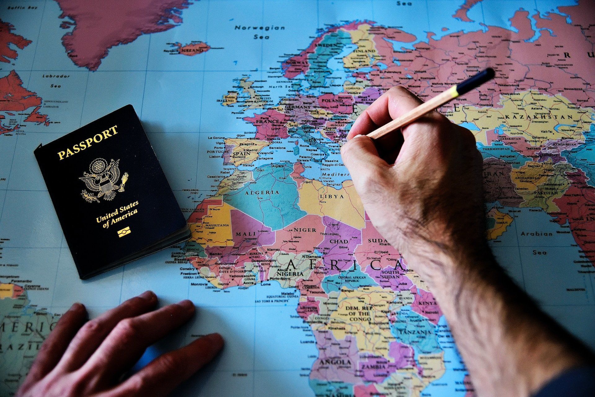 Térképen tollal jelölő kéz és útlevél
