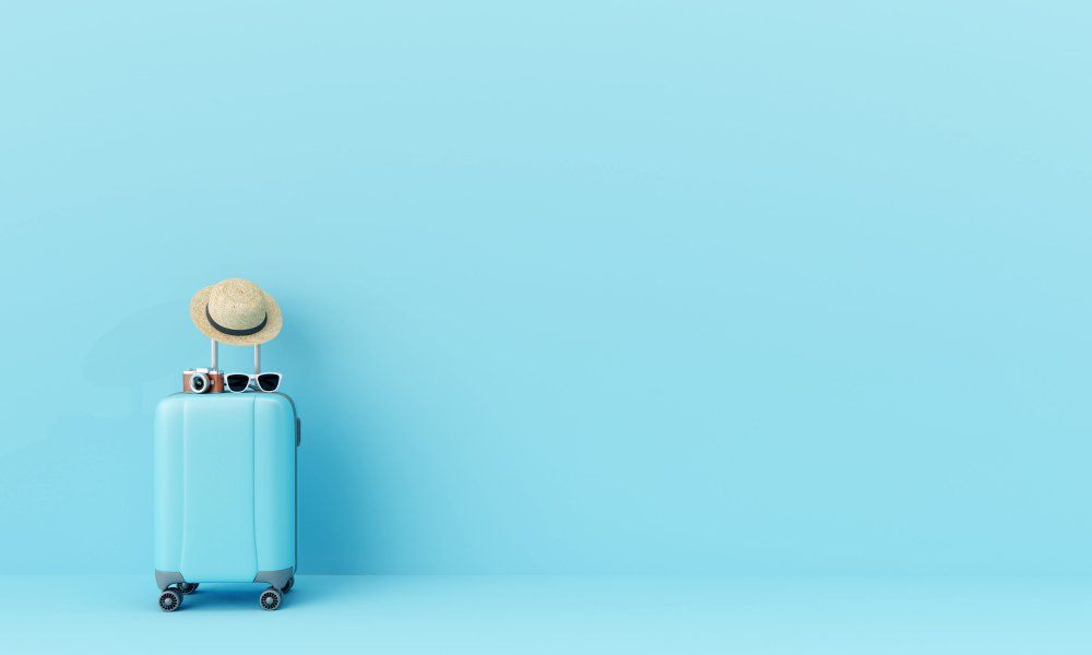 Kék bőrönd, tetején napszemüveg, kalap és fényképezőgép