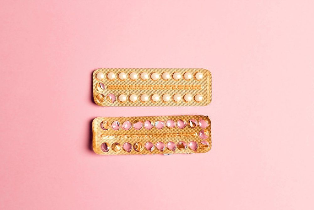 Női fogamzásgátló tabletták: üres és teli buborékfólia rózsaszín háttéren